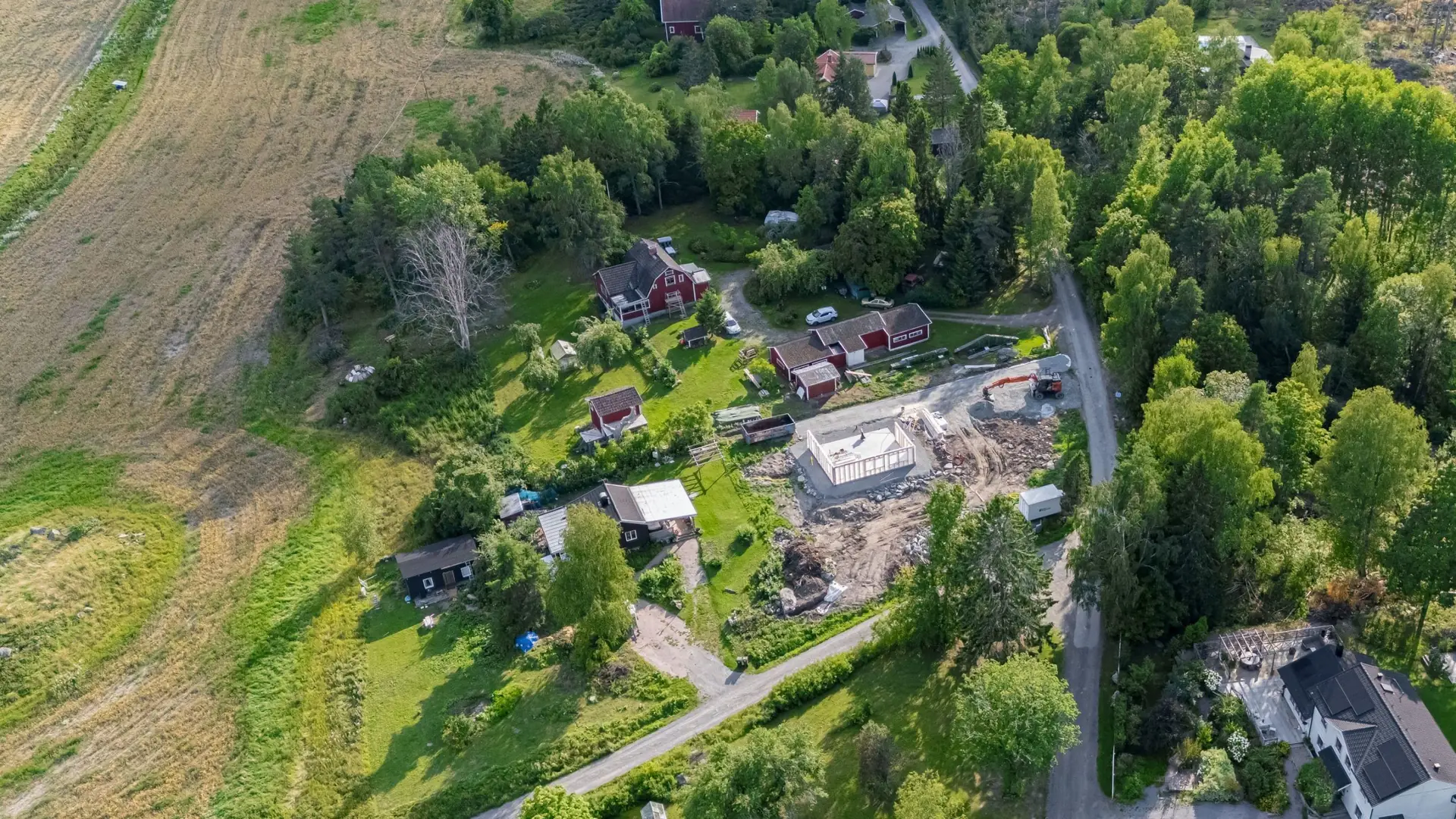 Flygbild över en tomt i skogskant med villor och åkermark runt omkring